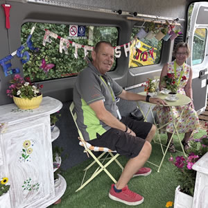Two people sat enjoying the flowers in the back of a bus.